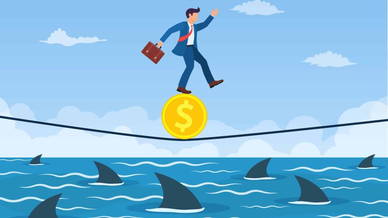 Dibujo de un hombre con traje y portafolio que va sobre una moneda en una cuerda en el aire. Está en medio del mar con tiburones. Busca estabilidad financiera